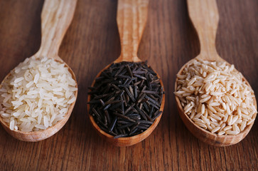 Different kinds of rice in spoons on wooden background