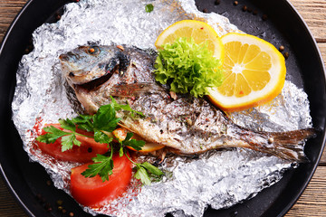 Tasty baked fish in foil on table close-up