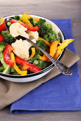 Frozen vegetables in bowl on napkin, on wooden table background