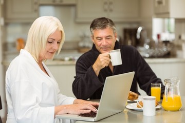 Mature couple having breakfast together woman using laptop