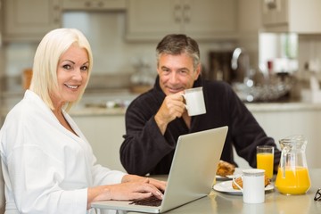 Fototapeta na wymiar Mature couple having breakfast together woman using laptop