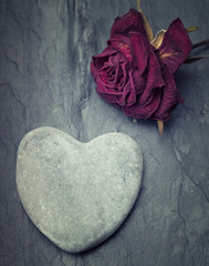 Fototapeta premium Grey zen heart shaped rock with a half dead rose on a tile backg