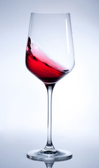 Red wine splashing in the elegant glass on gray