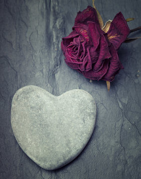 Grey zen heart shaped rock with a half dead rose on a tile backg