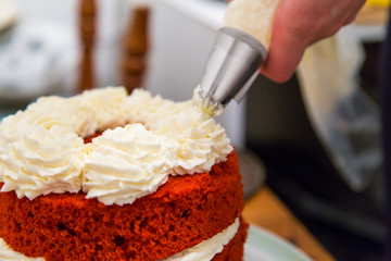 Close-up hand decorating red velvet cake with whipped cream