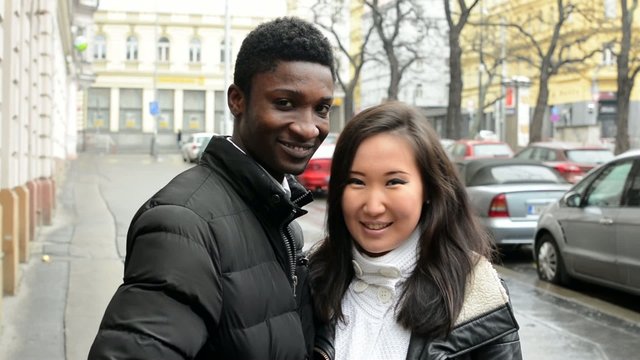 Happy couple kiss and smile to camera - black man, asian woman
