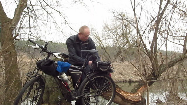 Adult  man  cyclist eats outdoors near river