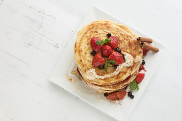 White plate full of pancakes with raspberries strawberries blueb