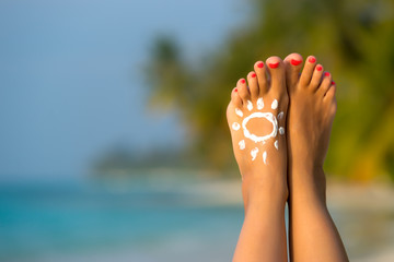 Woman foot with sun-shaped sun cream in the tropical beach conce