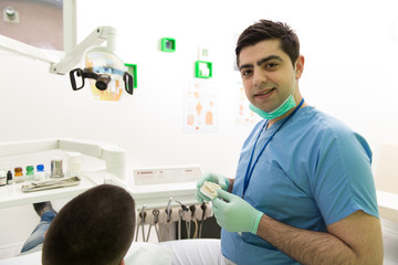 Dentist Explaining Artificial Teeth To Patient In Clinic