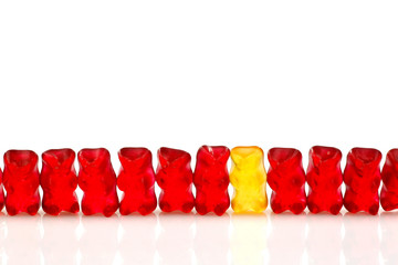 row of red gummy bears and a yellow one isolated on white