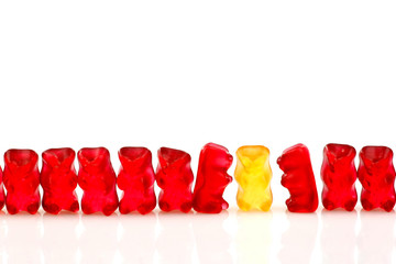 row of red gummy bears and a yellow one isolated on white