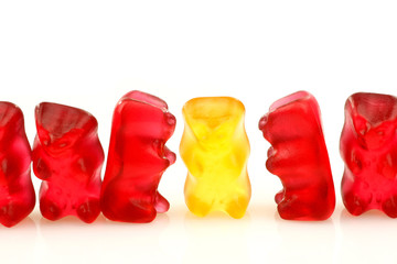 row of red gummy bears and a single yellow one on a white backgr