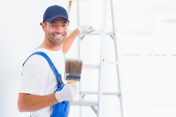 Happy handyman with paintbrush while climbing ladder