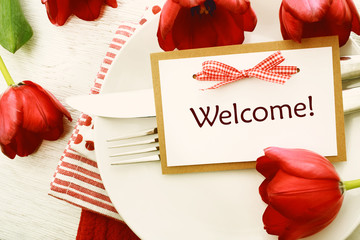 Dinner table setting with Welcome card and red tulips
