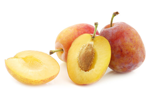 fresh ripe red and yellow plums and a cut one on a white backgro