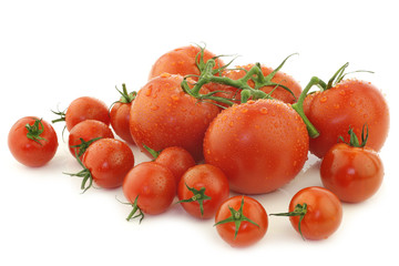 assorted tomatoes on the vine and cherry tomatoes on a white bac