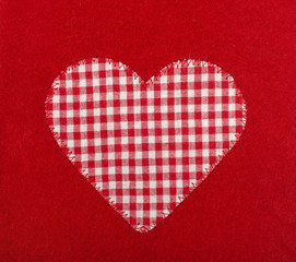 Checkered heart shape sewed on red wool background.
