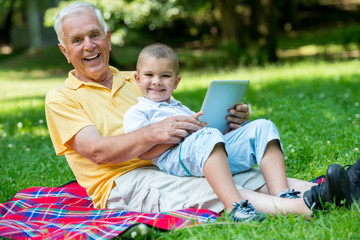 Naklejka na ściany i meble grandfather and child in park using tablet