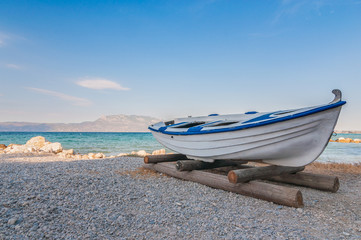 Fototapeta premium White fishing boat on sand with blue sky and water