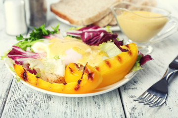 Toast with egg Benedict and greens on plate on wooden table