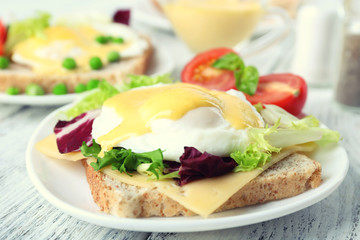 Toast with egg Benedict and tomato on plate on wooden table
