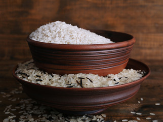 Grains of rice in bowls on wooden background