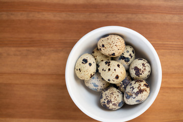 Quail eggs in white bowl on wooden table