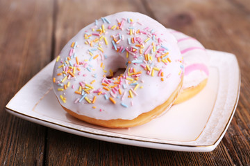 Delicious donuts with icing on plate on wooden background