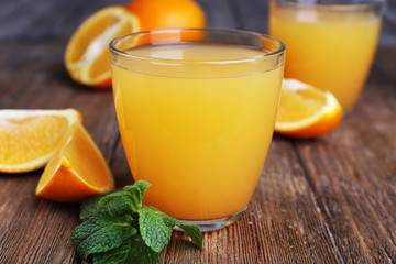 Glasses of orange juice with oranges on wooden table close up