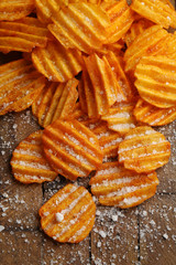 Delicious potato chips with salt on wooden table close-up