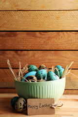 Bird colorful eggs in bowl on wooden background