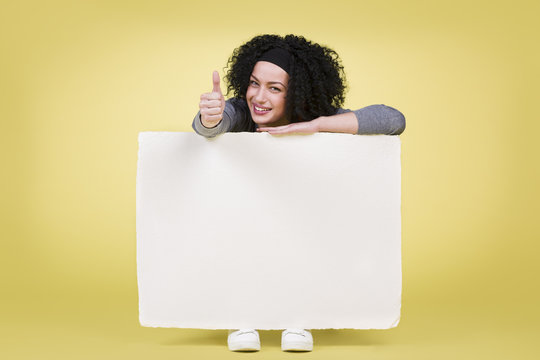 Smiling woman holding a white sign board showing thumbs up