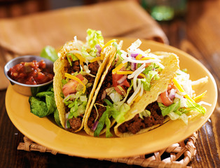 platter of three beef mexican tacos with cheese and lettuce