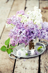 Bouquet of lilac flowers in vase on wooden background, toned