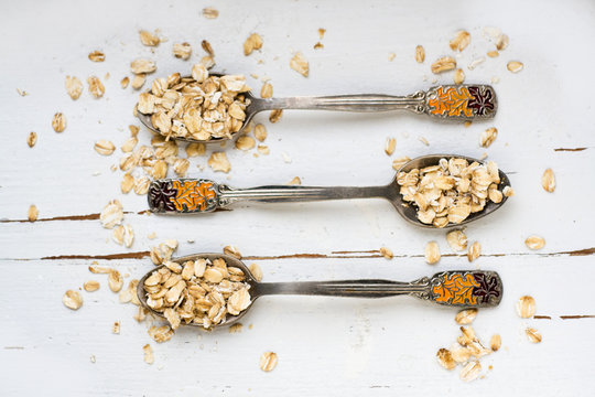 Three tablespoons of oatmeal lying on a white wooden background