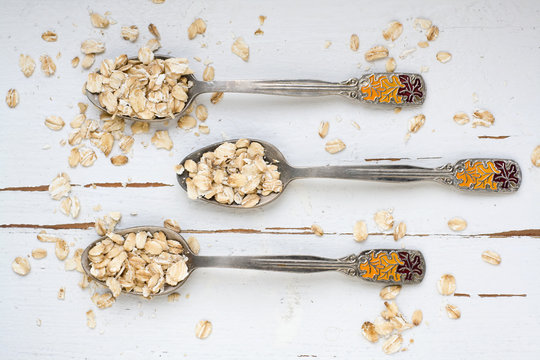 Three tablespoons of oatmeal lying on a white wooden background