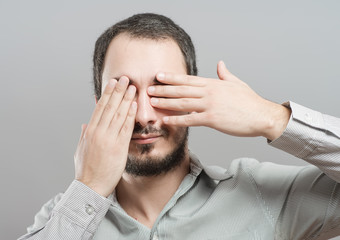 Fototapeta premium Portrait of a young man covering his eyes with hands