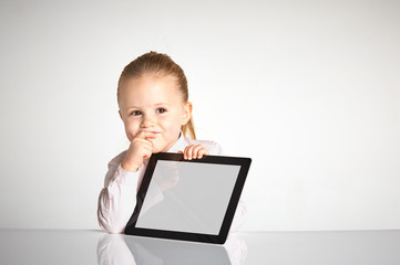 Cute little and smiling girl plays with a tablet