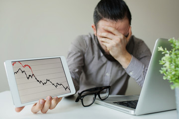 Depressed businessman leaning head below bad stock market chart