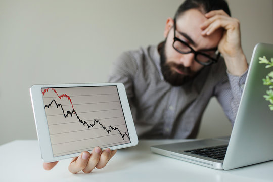 Depressed businessman leaning head below bad stock market chart