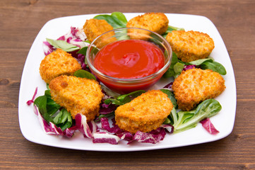 Nuggets of chicken over salad on wooden table
