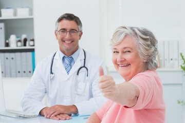 Patient showing thumbs up sign while sitting with doctor