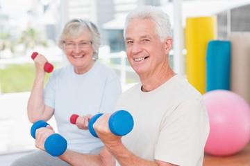 Happy senior couple lifting dumbbells in gym