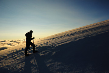 girl goes on a snowy slope in the mountains against sun