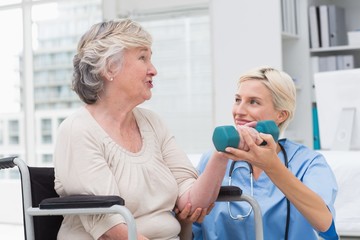 Nurse looking at patient while assisting her in lifting dumbbell
