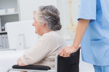 Nurse pushing senior patient in wheelchair at clinic