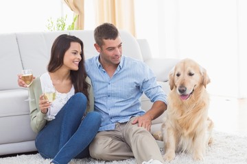 Couple holding wine glasses while looking at dog