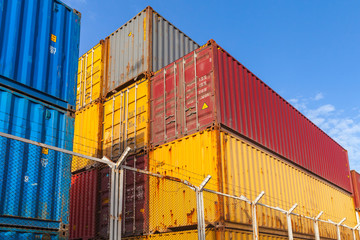 Colorful cargo containers are stacked behind metal fence