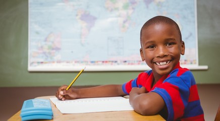 Cute little boy writing book in classroom